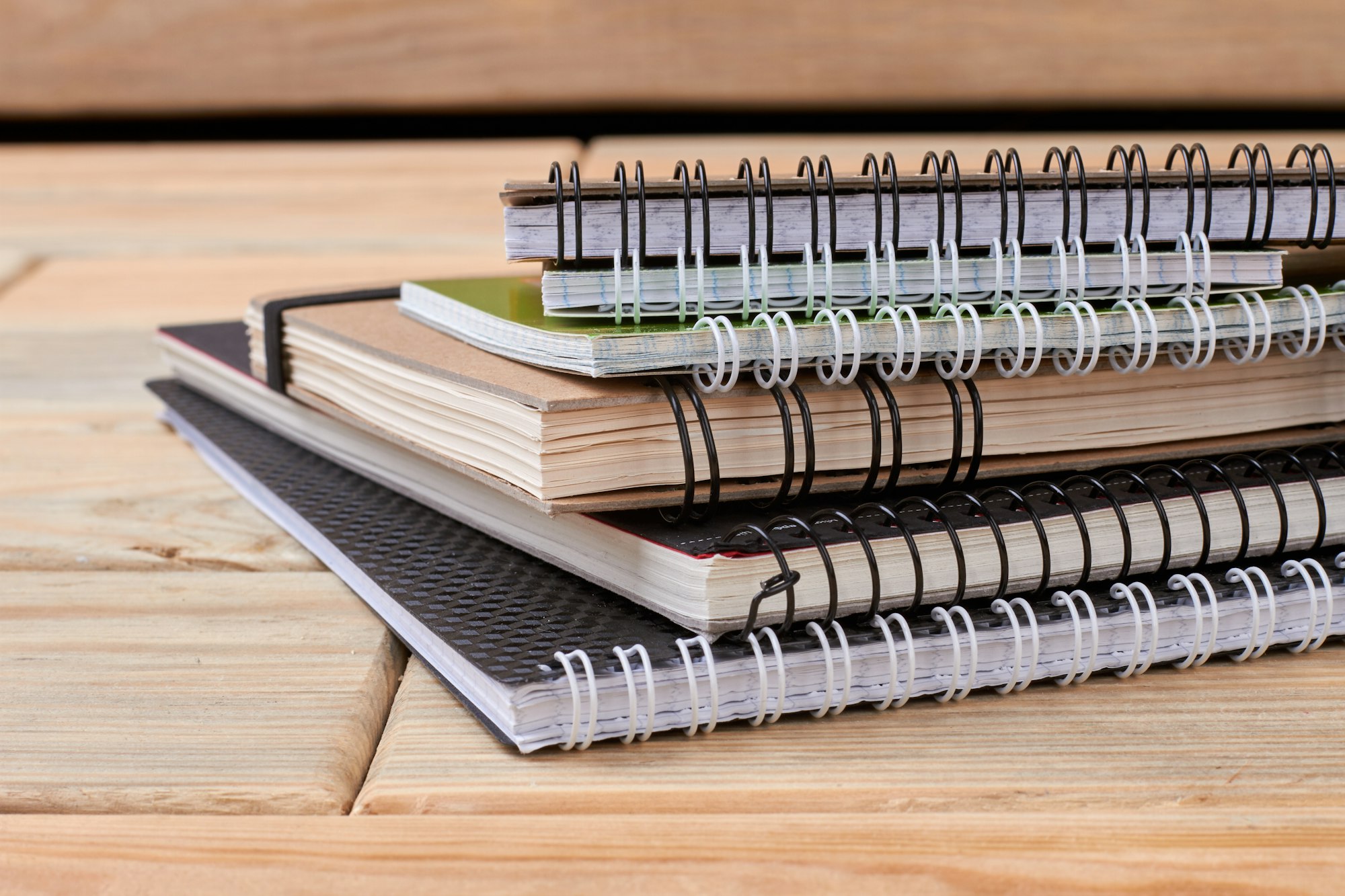 Stack of spiral notebooks on wooden background.