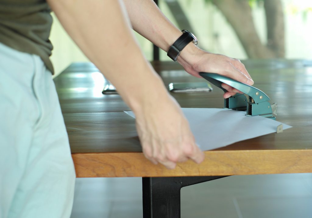 Closeup hands of worker drilling the paper by using the steel puncher in the modern office